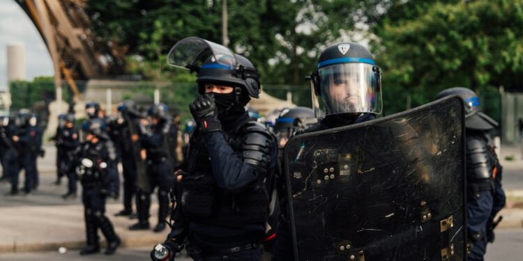 Riot police officers holding shields in an urban street, used as contextual imagery for France's recent unrest.